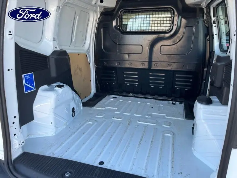 Vue intérieure arrière du fourgon Ford Transit Courier blanc Glacier, montrant la cloison grillagée et l'espace de chargement vide.