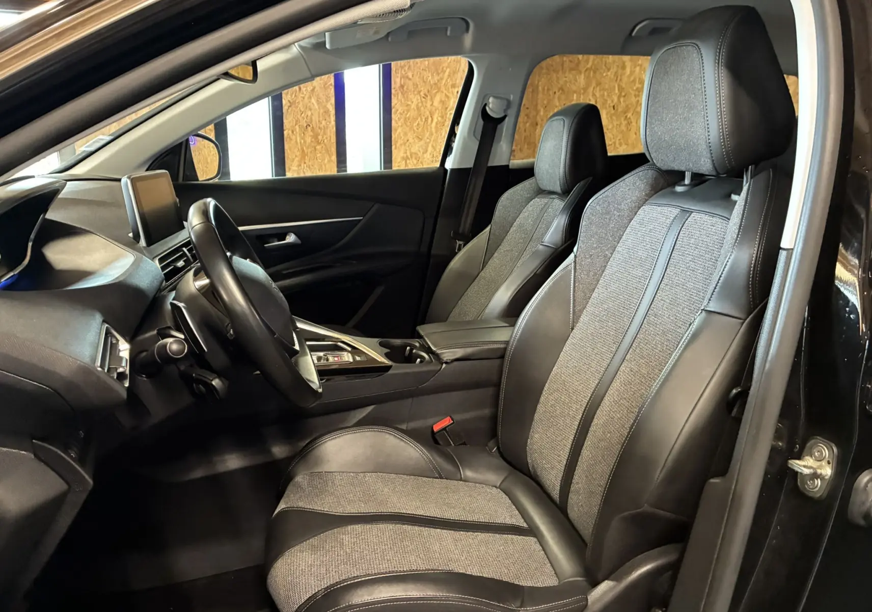 Vue intérieure côté conducteur du Peugeot 3008 noir, montrant les sièges tissu et cuir ainsi que le tableau de bord moderne.