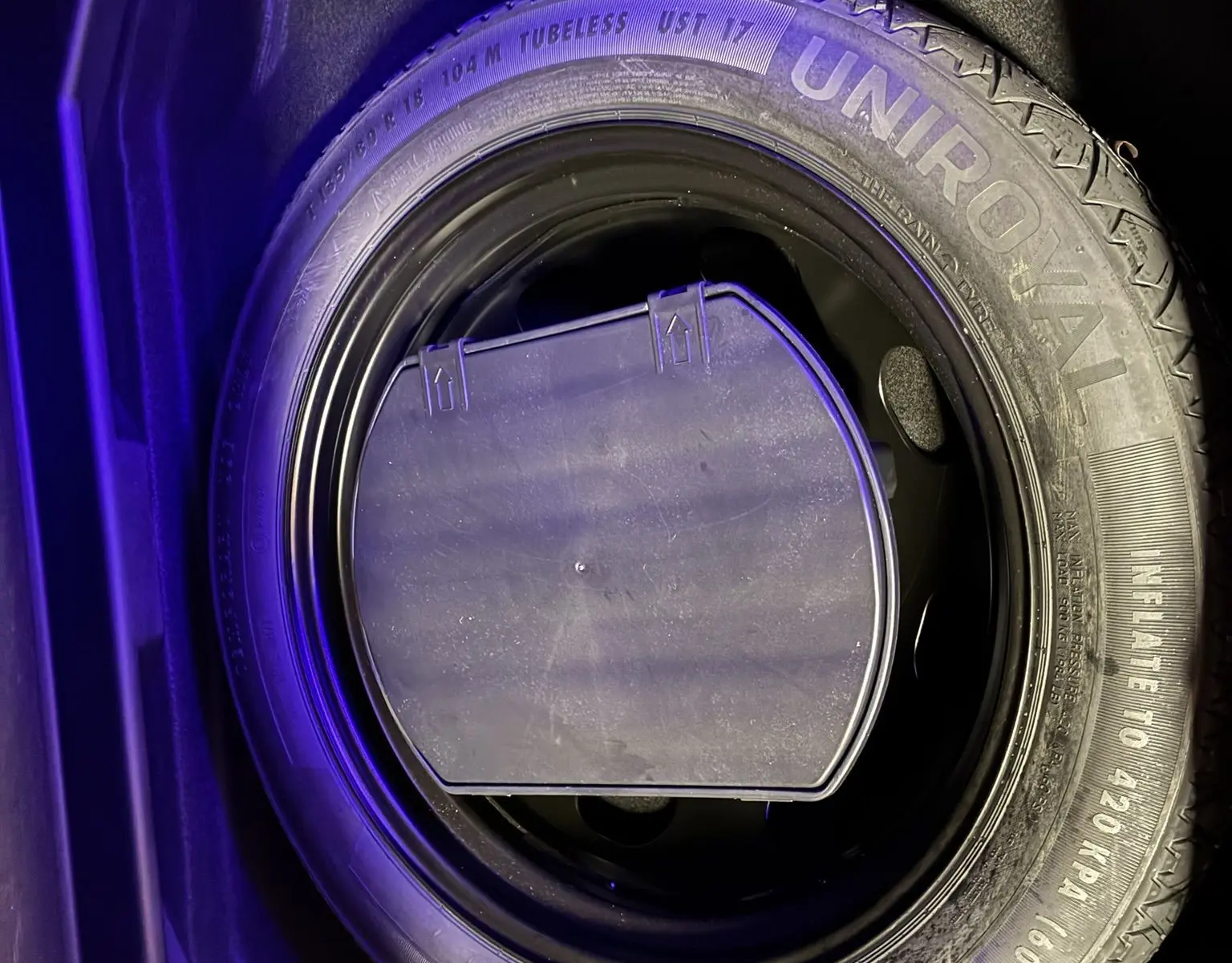 Gros plan sur la roue de secours noire Uniroyal dans le coffre d’un Peugeot 3008 noir, éclairage violet.