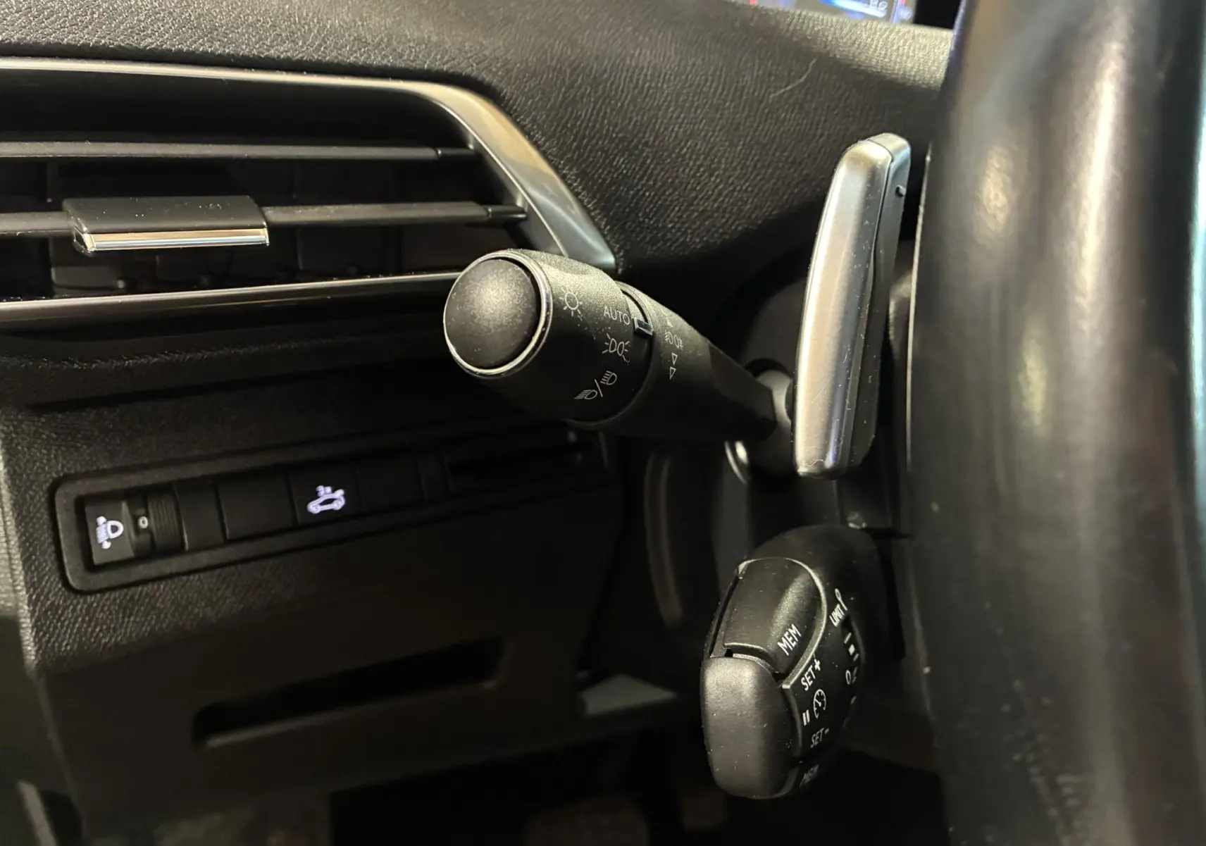 Gros plan sur les commandes au volant côté gauche du Peugeot 3008 noir, mettant en valeur les leviers de clignotants et régulateur de vitesse.