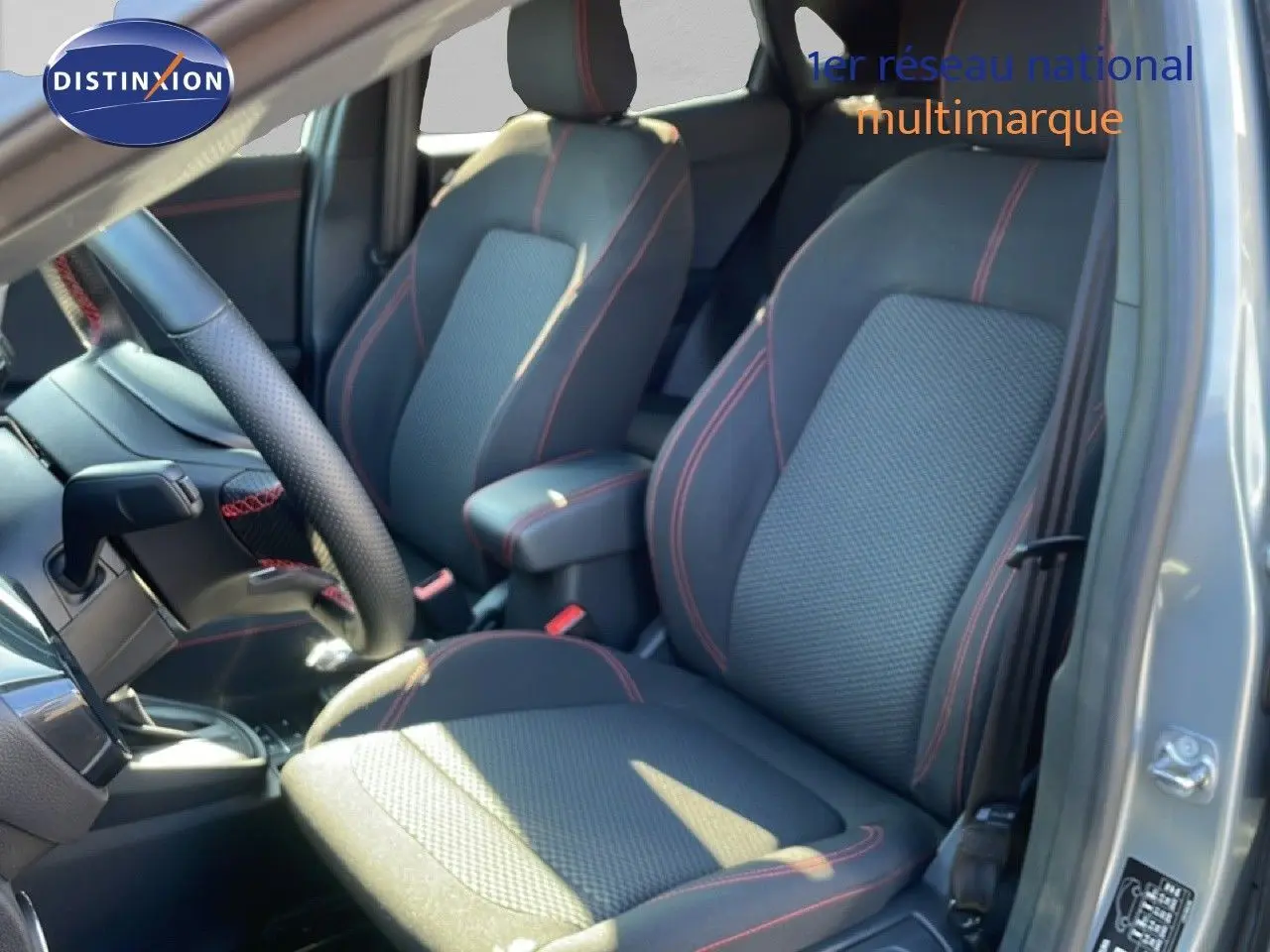 Vue intérieure côté conducteur du Ford Puma 2023, sièges tissu noir avec surpiqûres rouges et volant cuir perforé.