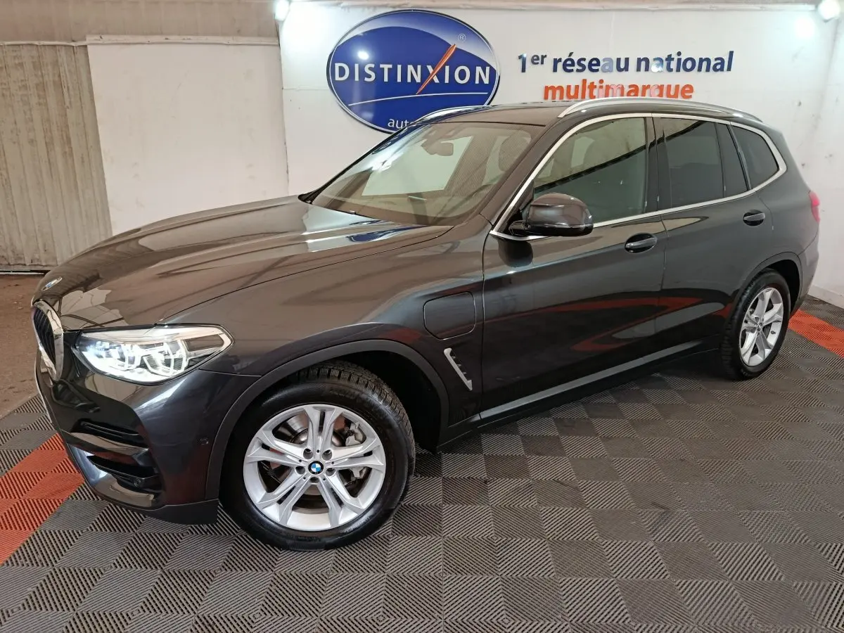 BMW X3 xDrive30e gris foncé vue 3/4 avant droit avec phares allumés dans un showroom intérieur.