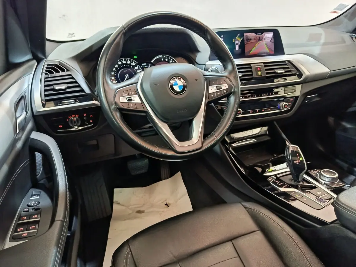 Vue intérieure avant du BMW X3 xDrive30e 2020, volant cuir multifonctions, tableau de bord avec écran de navigation et caméra de recul.