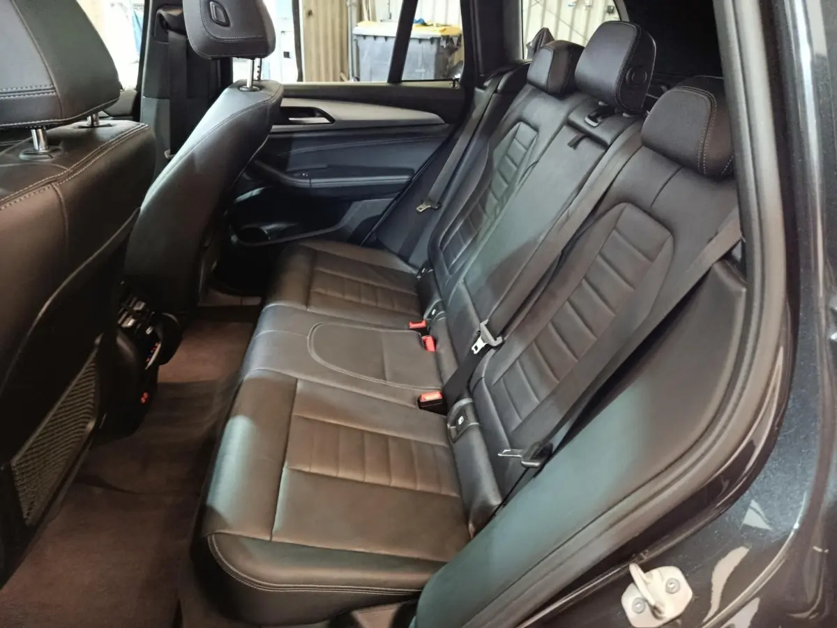 Vue intérieure côté droit des sièges arrière en cuir noir du BMW X3 xDrive30e gris foncé, avec ceintures et appuie-têtes visibles.