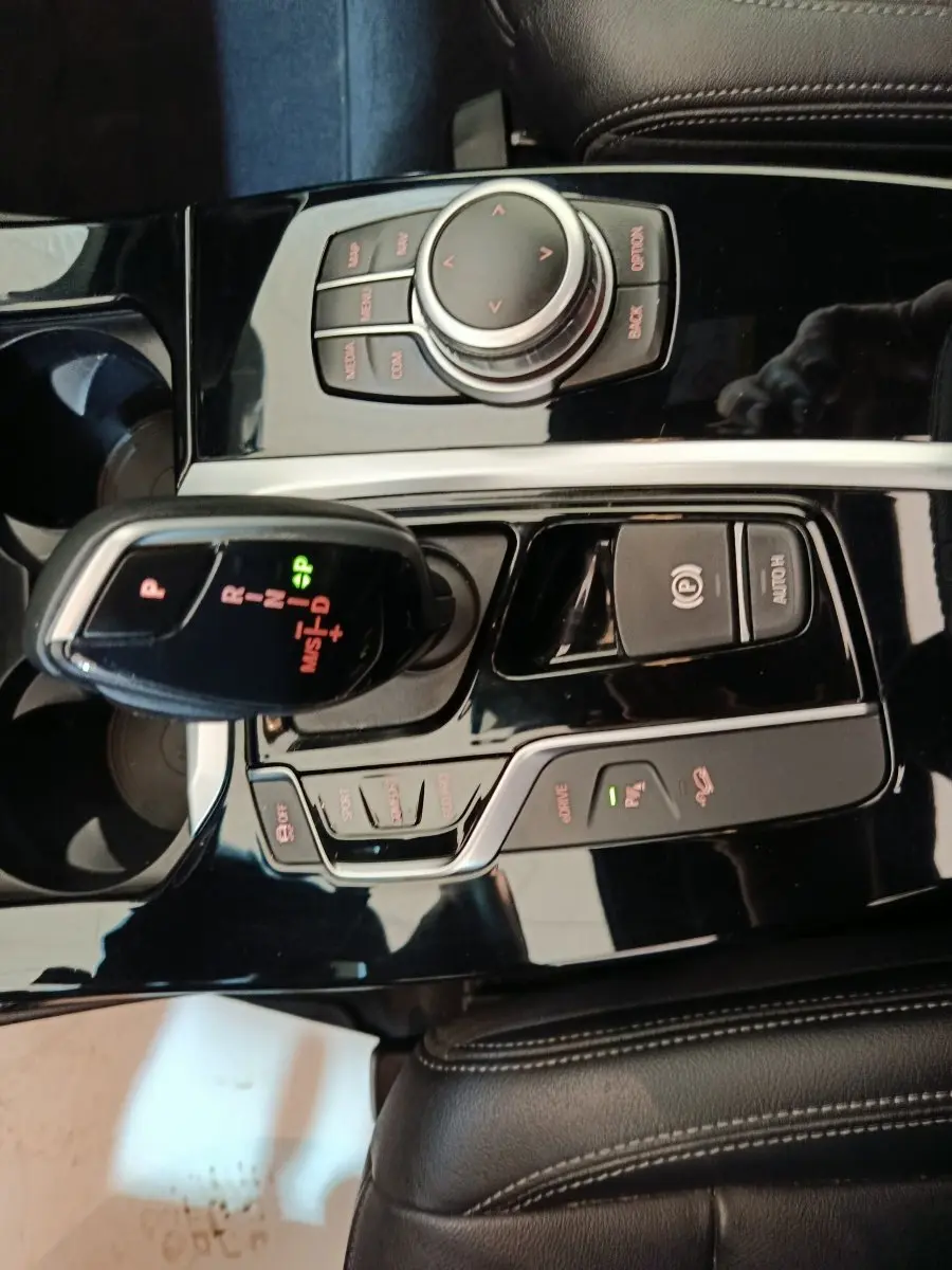 Vue rapprochée de la console centrale noire brillante du BMW X3 xDrive30e avec levier de vitesses et molette de contrôle.