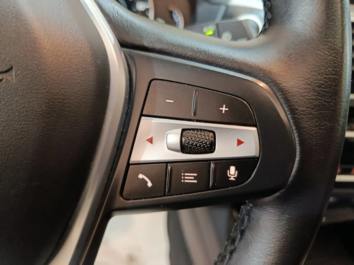 Gros plan sur les commandes multifonctions en cuir noir du volant BMW X3 xDrive30e 2020, boutons de volume et appel.