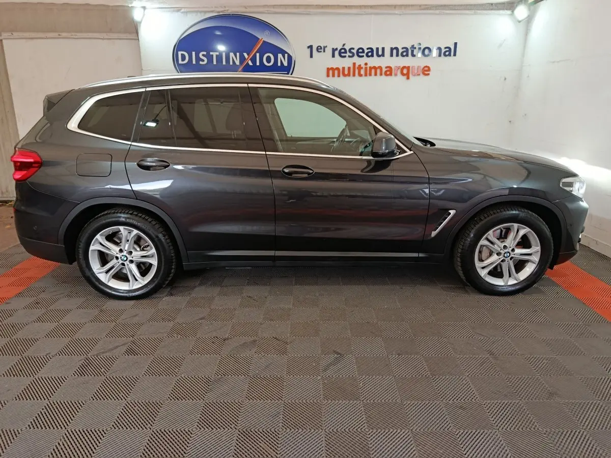 Vue profil côté gauche d’un BMW X3 xDrive30e gris foncé dans un showroom avec logo Distinxion en arrière-plan.