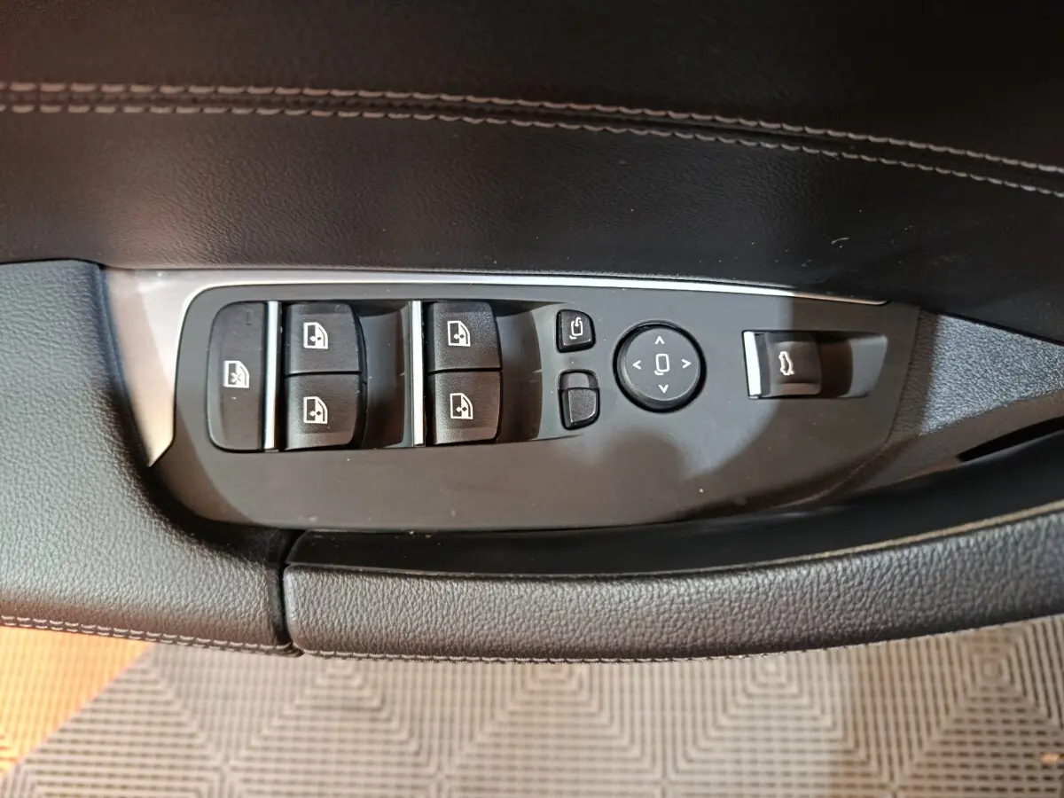 Gros plan sur les commandes de lève-vitres et rétroviseurs sur la porte côté conducteur du BMW X3 gris foncé.