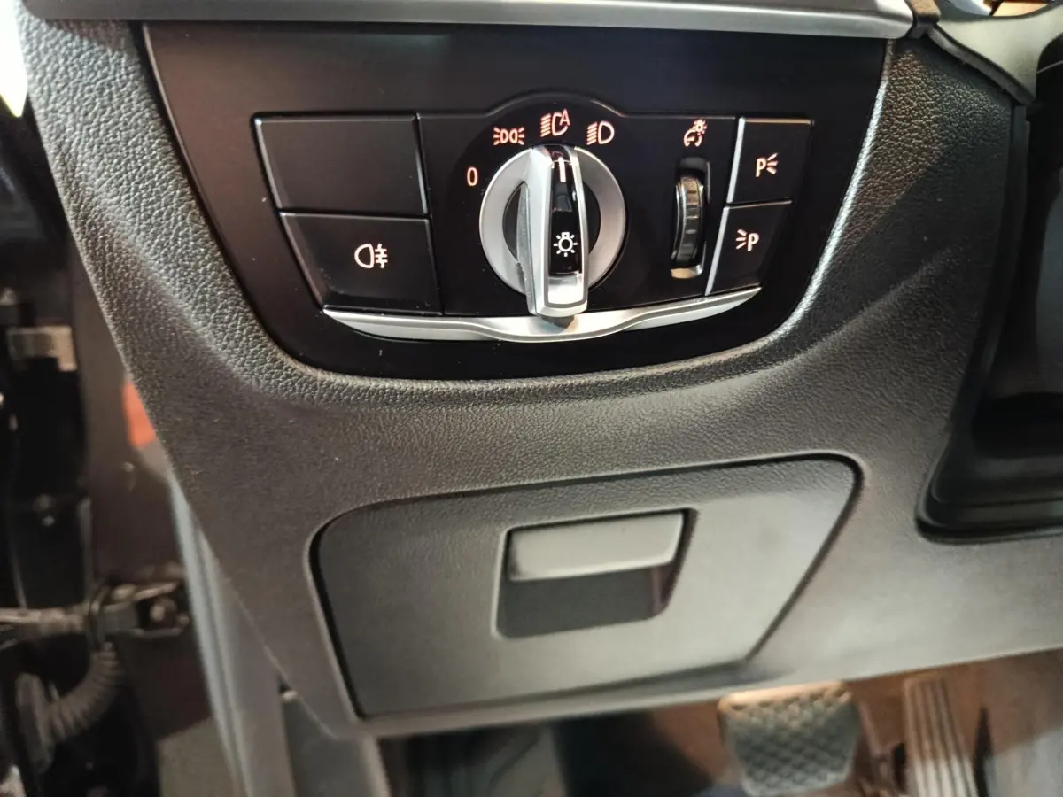 Gros plan sur le panneau de commande des phares et feux, intérieur noir du BMW X3 xDrive30e gris foncé.