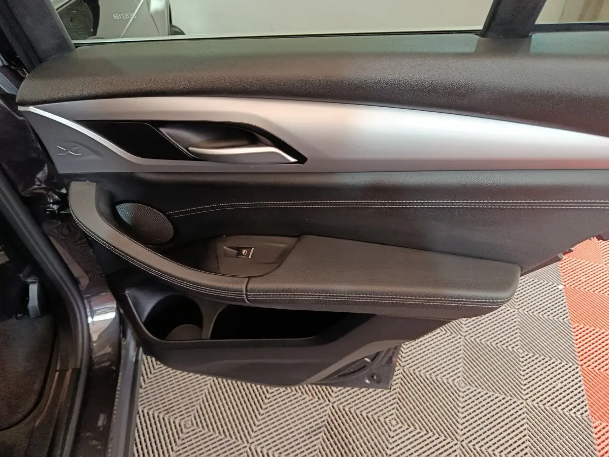 Vue intérieure côté gauche de la porte avant d’une BMW X3 gris foncé avec garniture noire et insert argenté.