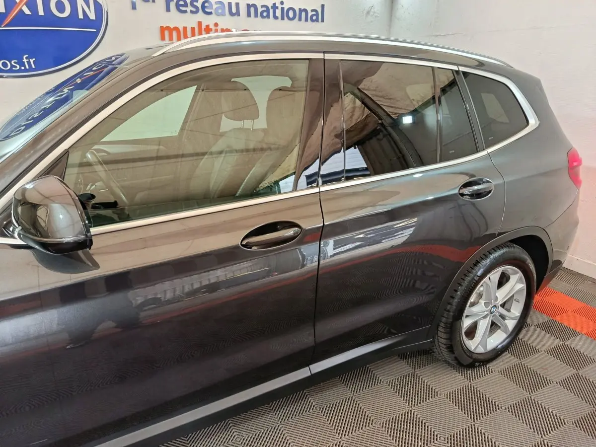 Vue latérale côté gauche d’un BMW X3 gris foncé avec jantes alliage et rails de toit chromés visibles.