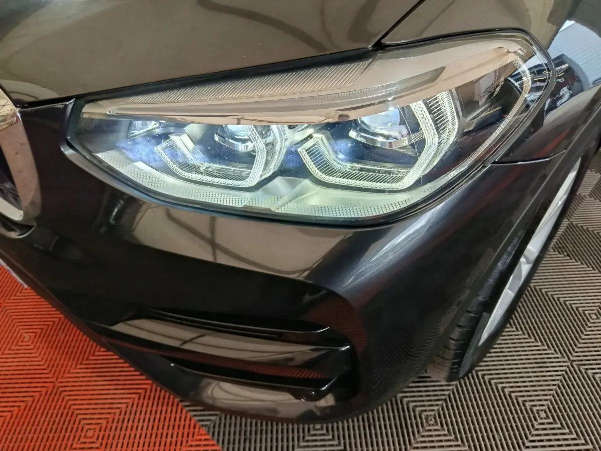 Gros plan sur le phare avant droit du BMW X3 xDrive30e gris foncé, mettant en valeur les détails LED et la carrosserie brillante.