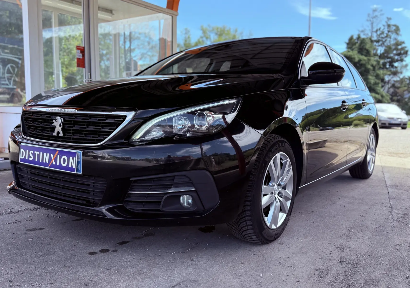 Peugeot 308 SW noire métal vue 3/4 avant droit sous abri avec jantes alliage et calandre distinctive