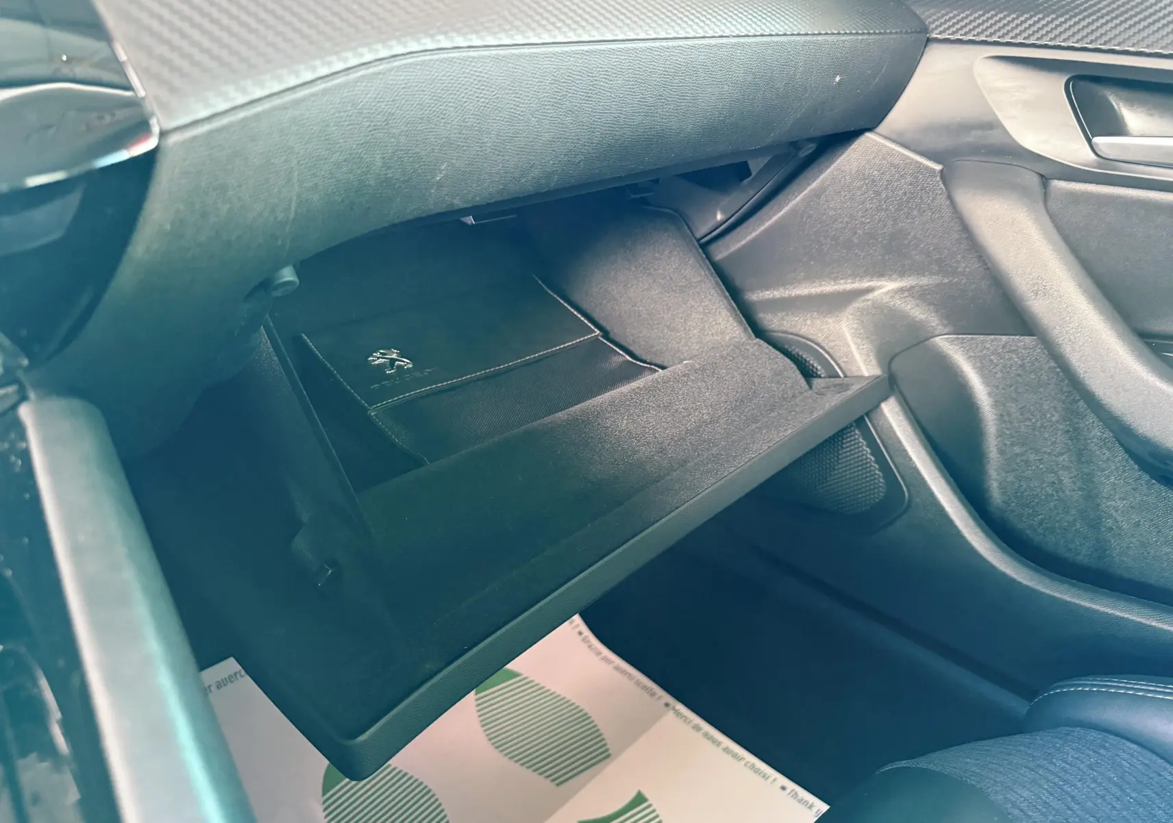Gros plan sur la boîte à gants ouverte côté passager d'une Peugeot 308 SW noire avec un livret Peugeot à l'intérieur.