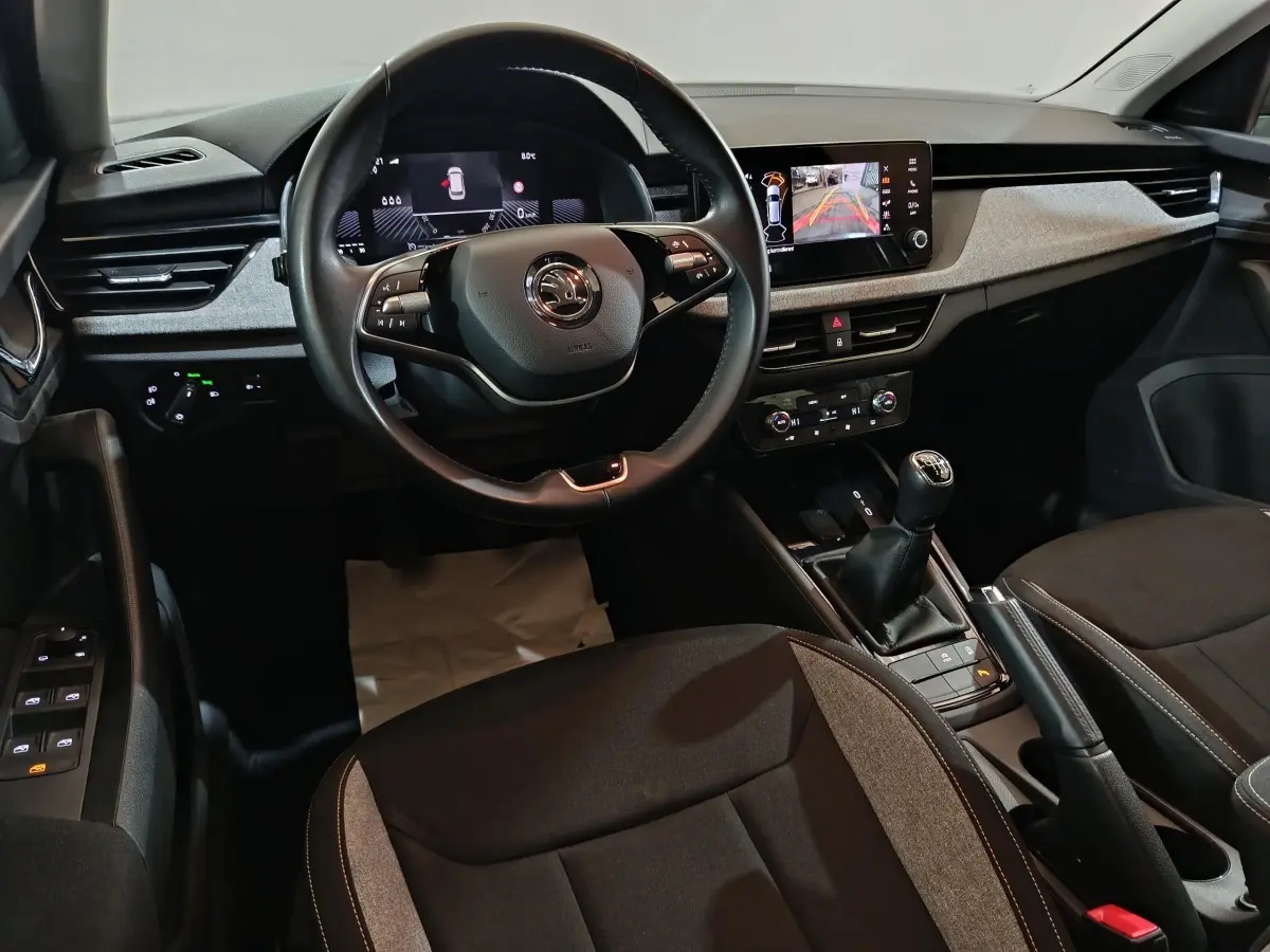 Intérieur avant du Skoda Kamiq 2024 gris clair, volant cuir multifonctions et écran tactile central avec caméra de recul.