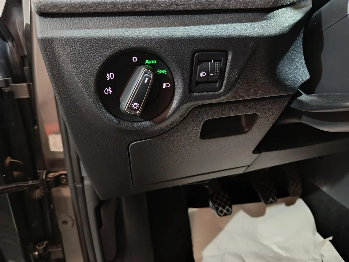 Gros plan sur le tableau de bord côté gauche du Skoda Kamiq gris clair 2024, montrant la commande des phares et réglage hauteur.