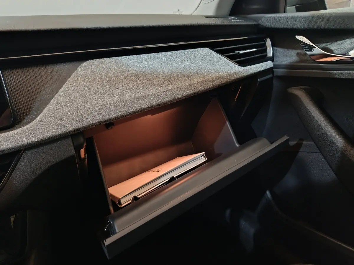 Vue intérieure côté passager du tableau de bord gris clair du Skoda Kamiq 2024 avec boîte à gants ouverte et manuel visible.