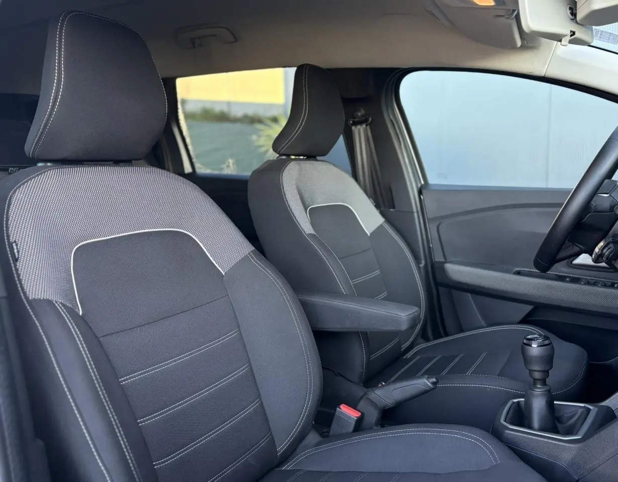 Vue intérieure côté droit du Dacia Jogger 2025, montrant les sièges avant noirs avec surpiqûres blanches et levier de vitesse manuel.