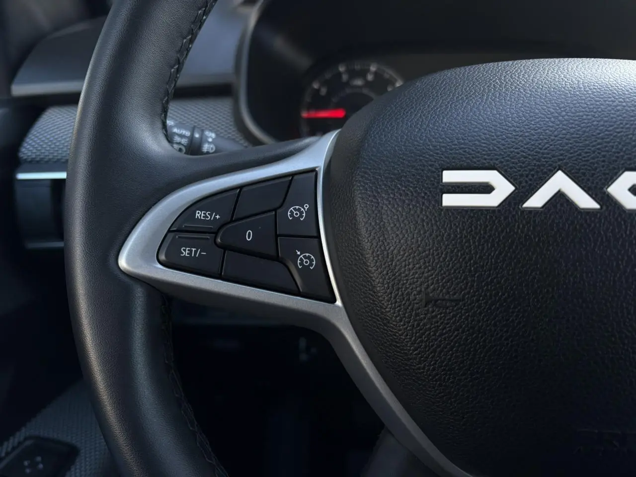 Gros plan sur le volant noir du Dacia Jogger 2025, avec commandes de régulateur de vitesse et logo DACIA visible.