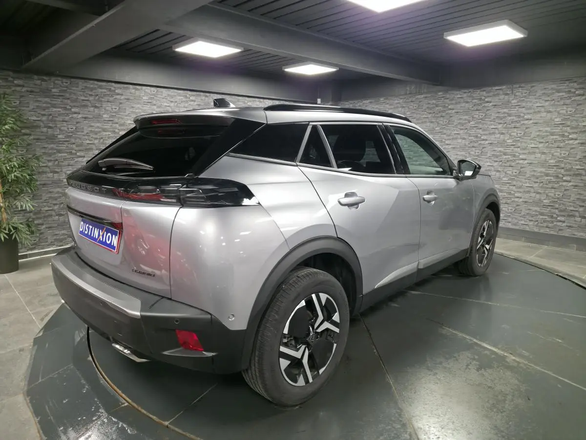 Vue 3/4 arrière droite d'un Peugeot 2008 gris métallisé avec jantes alliage bi-ton et toit noir en intérieur showroom.
