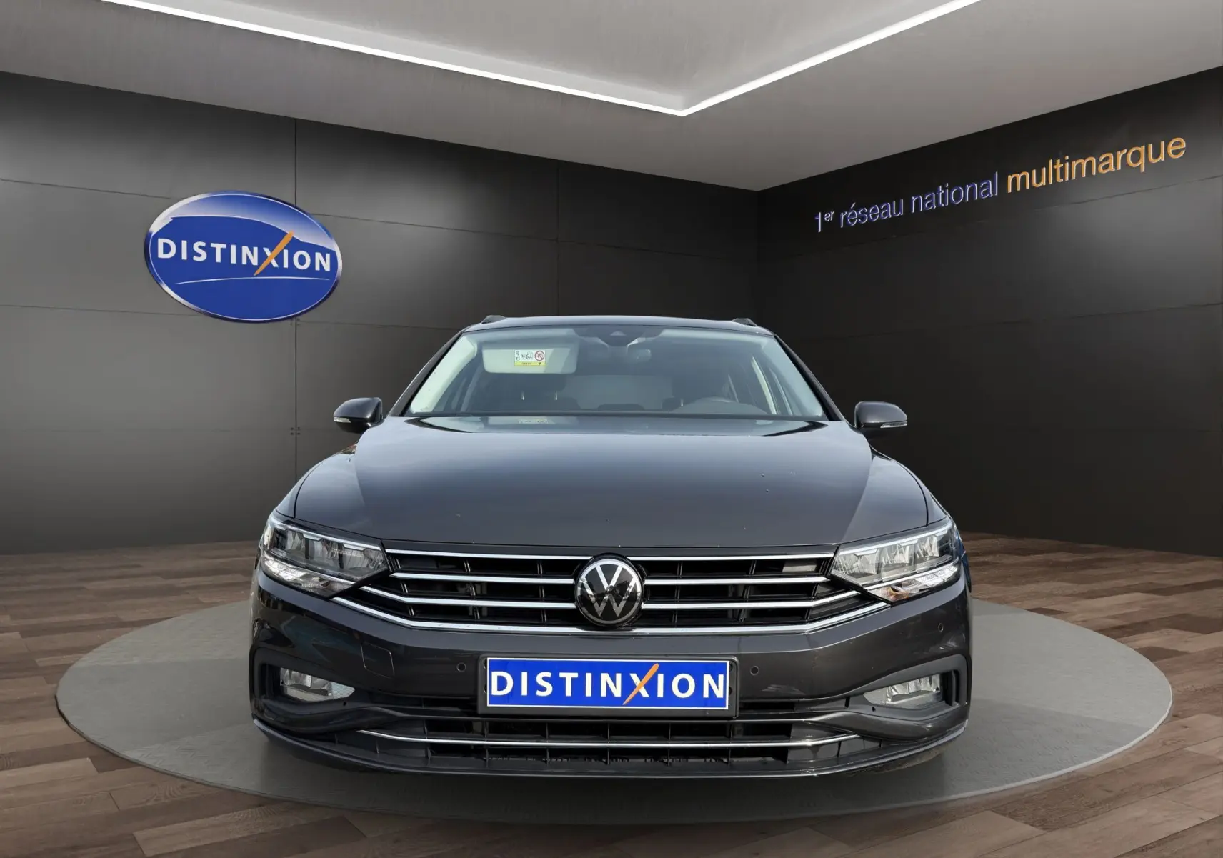 Vue frontale d'une Volkswagen Passat gris foncé, avec calandre chromée et phares LED, en showroom Distinxion.