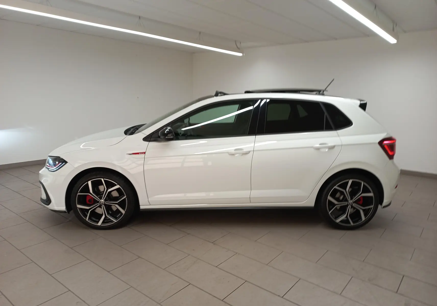 Vue de profil côté gauche d'une Volkswagen Polo GTI blanche avec toit ouvrant noir et jantes 18 pouces en alliage.