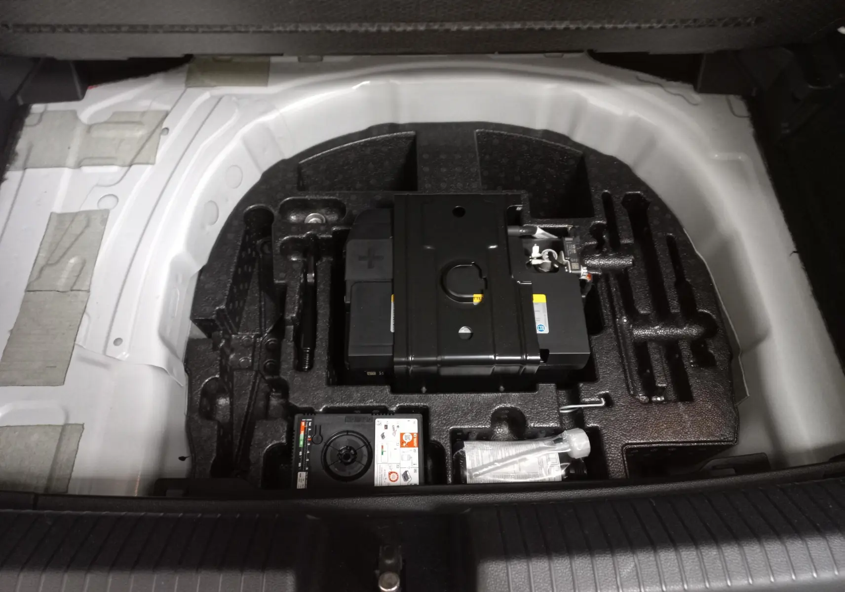 Vue plongeante sur le coffre ouvert d'une Volkswagen Polo blanche, montrant le compartiment à outils et la batterie de secours.