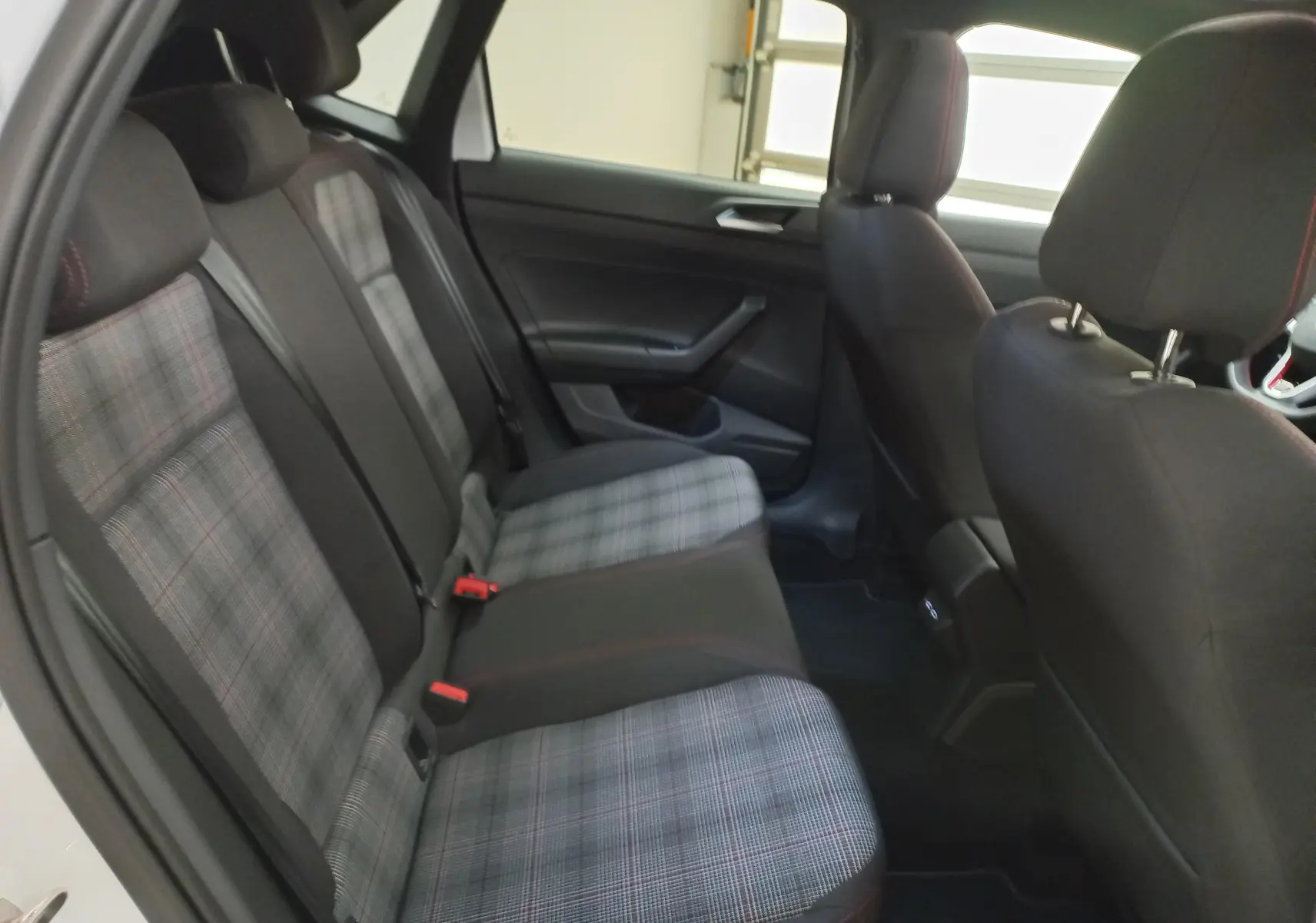 Vue intérieure côté gauche des sièges arrière d'une Volkswagen Polo GTI 2024 avec sellerie à motif écossais et surpiqûres rouges.