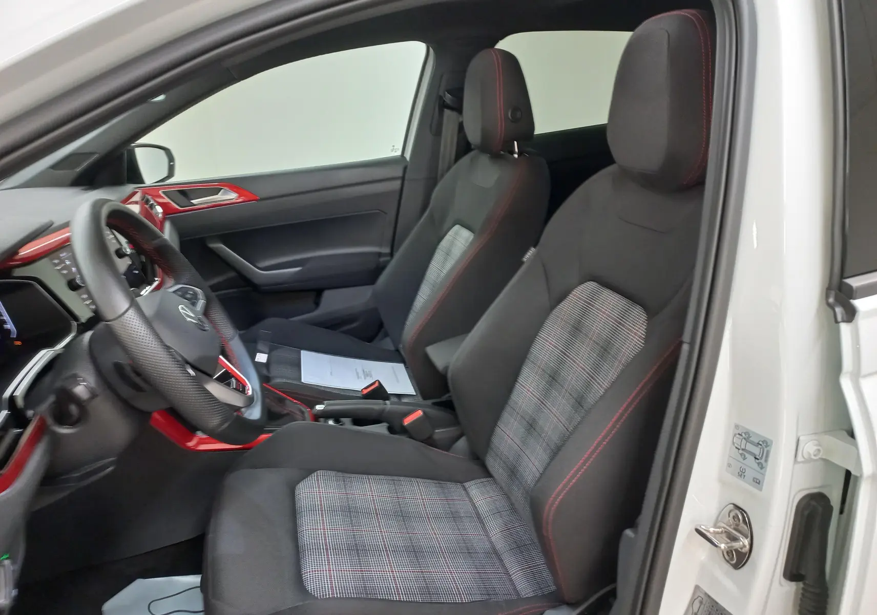 Vue intérieure côté conducteur d'une Volkswagen Polo GTI blanche avec sièges sport à motif écossais et surpiqûres rouges.