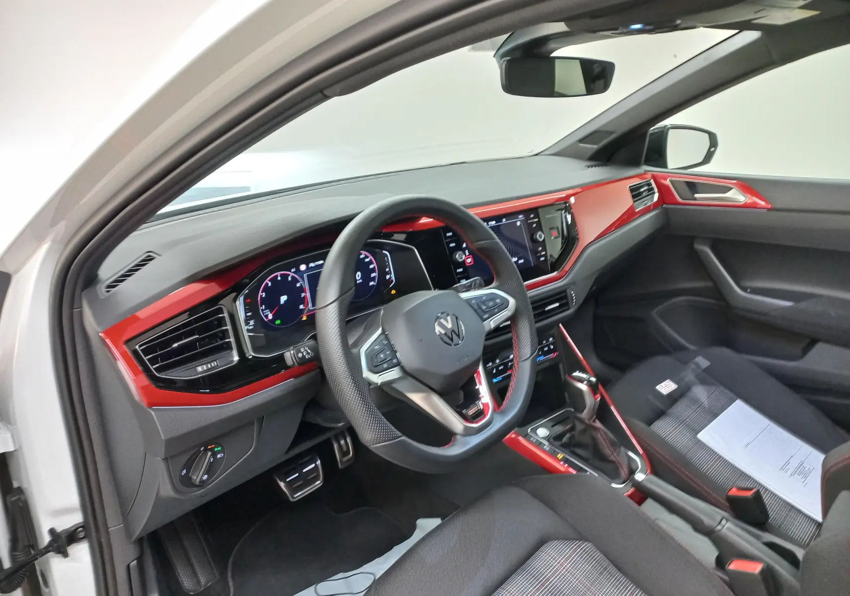 Vue intérieure côté conducteur de la Volkswagen Polo GTI 2024 avec tableau de bord rouge et volant multifonction.