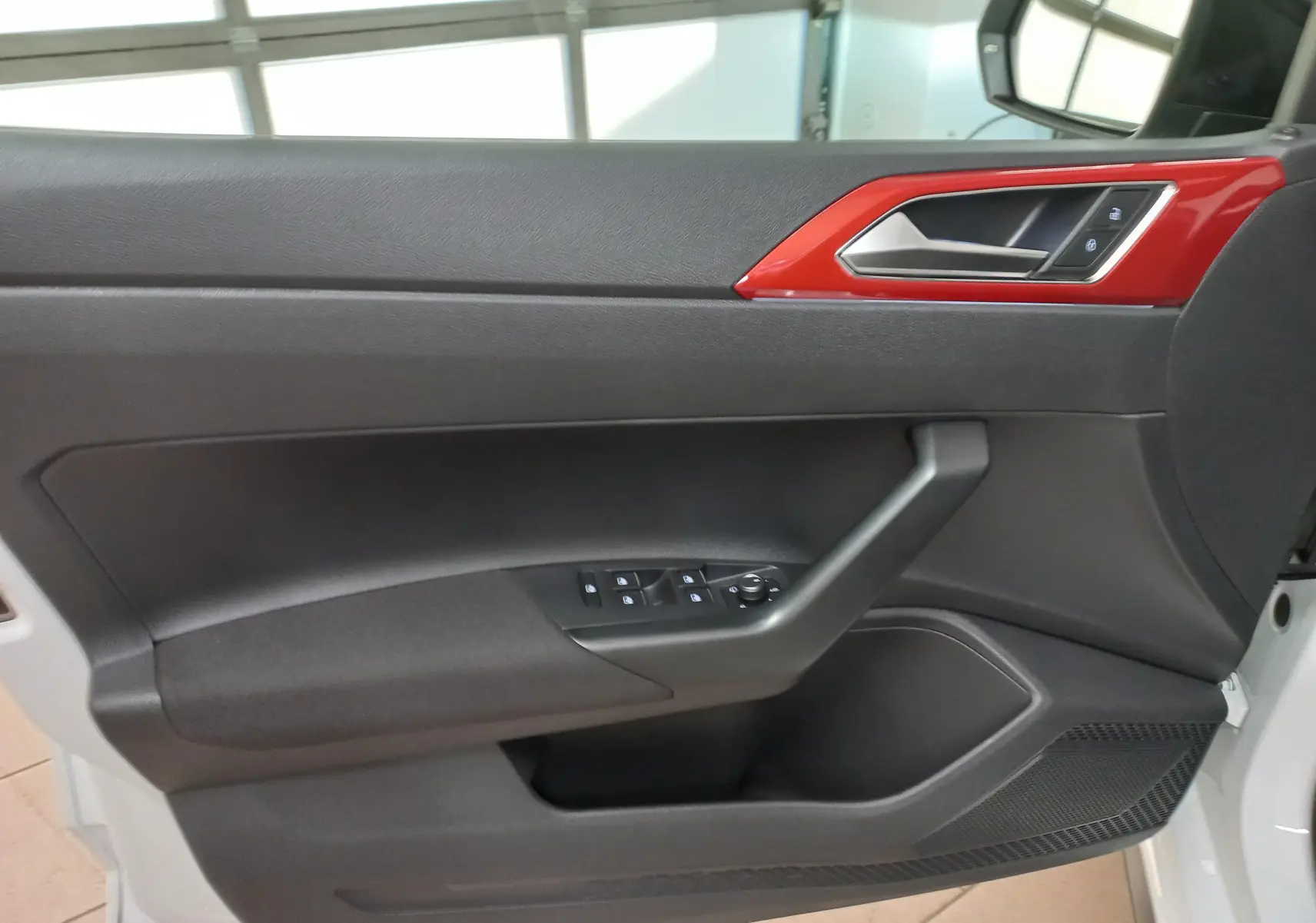 Vue intérieure côté gauche de la porte d'une Volkswagen Polo GTI 2024 blanche avec insert rouge et commandes de vitres.