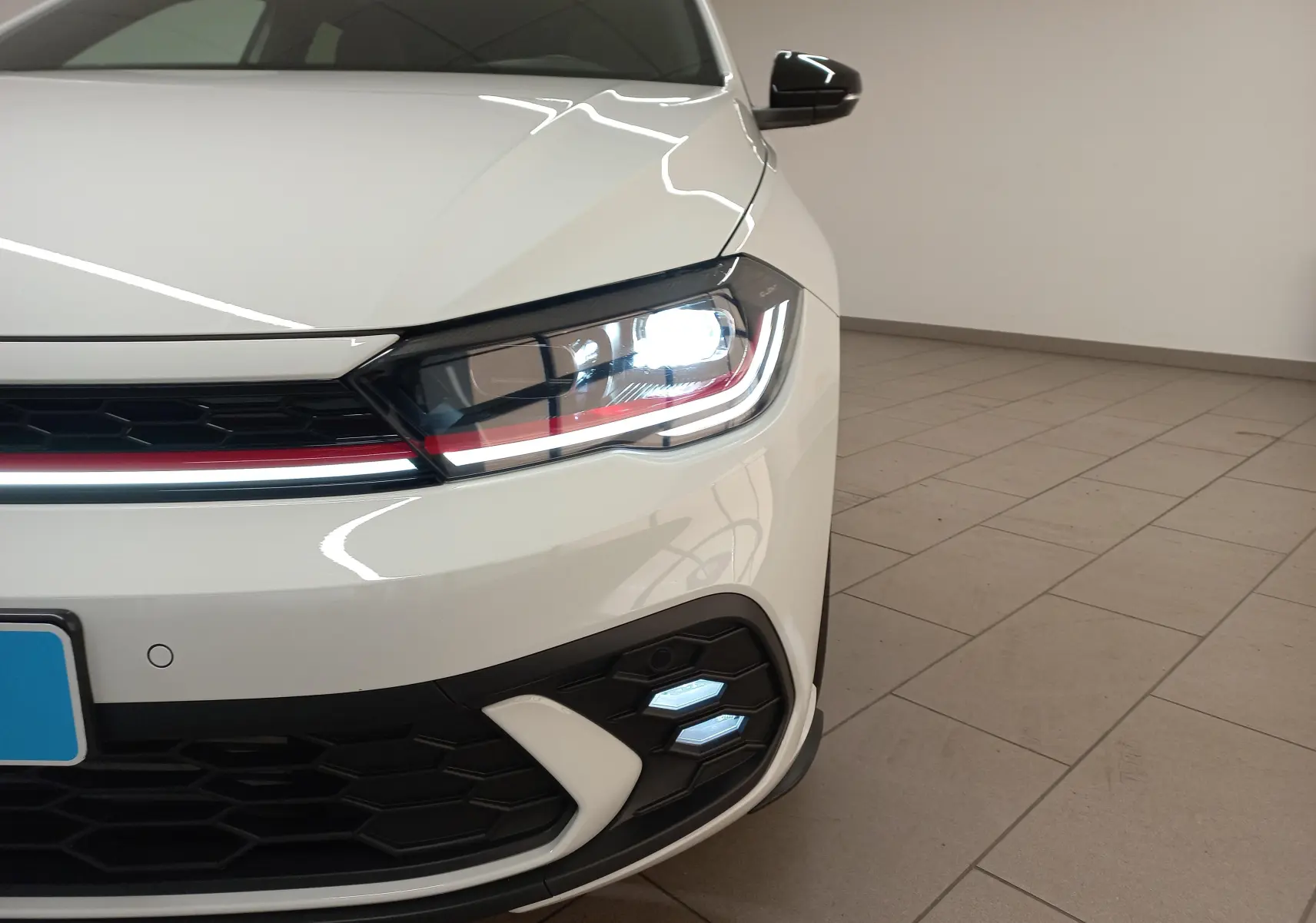 Gros plan sur l'avant droit blanc pur d'une Volkswagen Polo 2.0 TSI GTI 2024 avec phare LED et bandeau rouge distinctif.