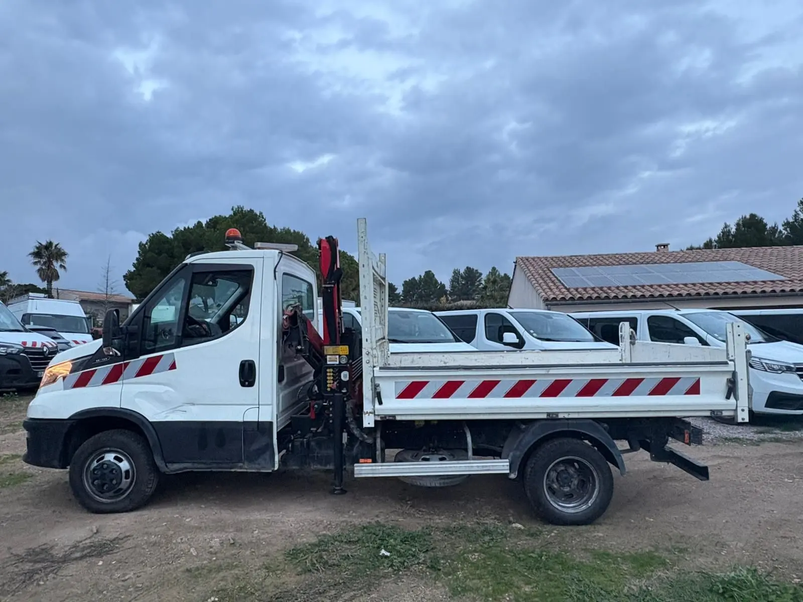 IVECO Daily Chassis Cabine blanc vu de profil gauche avec benne et grue Palfinger rouge et stabilisateurs déployés.