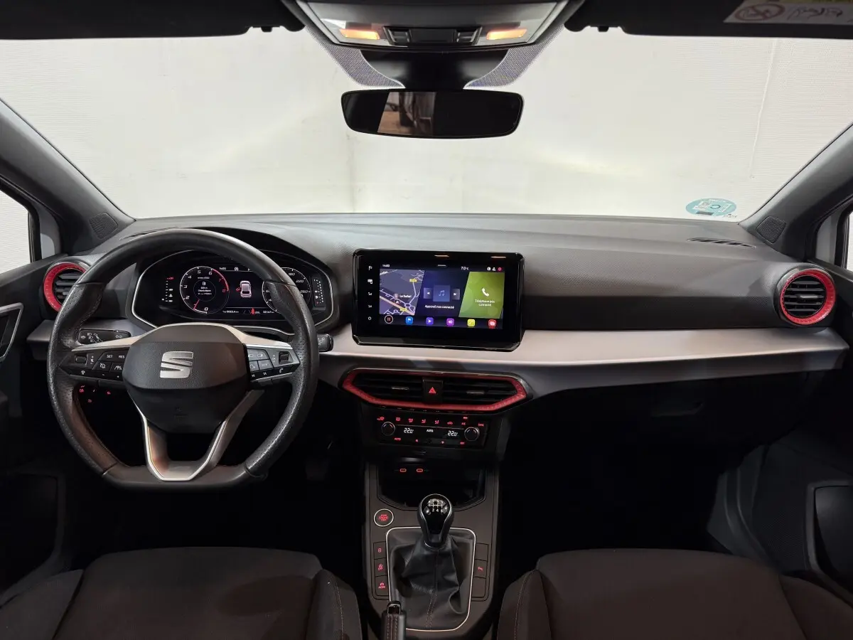 Vue frontale de l'intérieur de la SEAT Ibiza 1.0 TSI 110 FR 2024, volant cuir, écran tactile et détails rouges sur aérateurs.