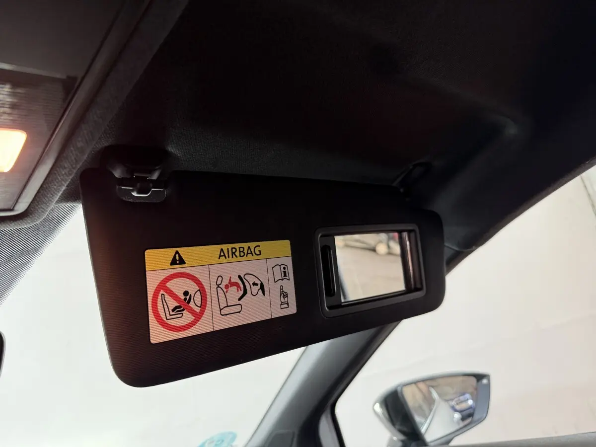 Détail du pare-soleil côté conducteur avec miroir intégré et avertissement airbag, rétroviseur extérieur visible.