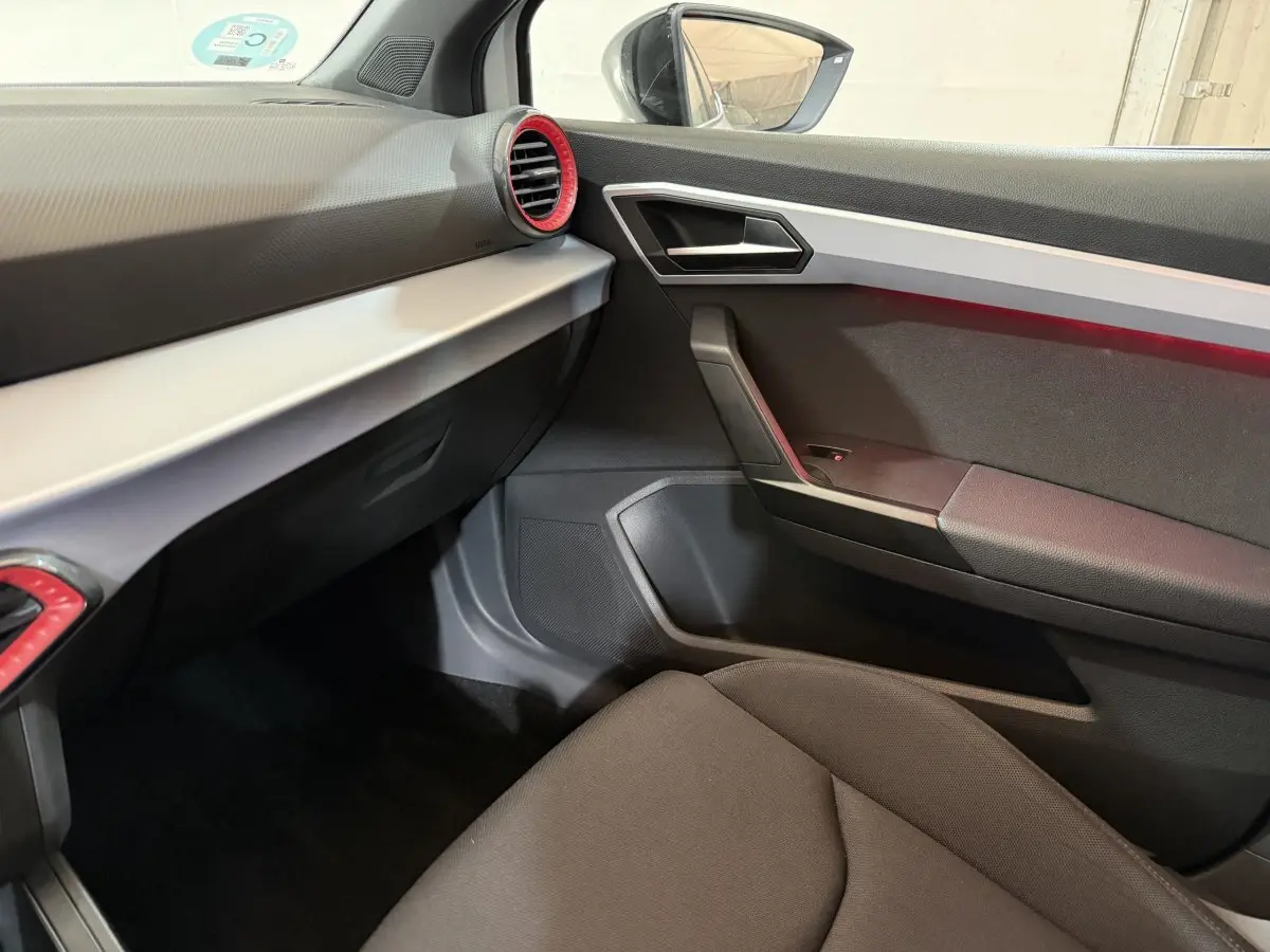 Vue intérieure côté passager de la SEAT Ibiza 2024, avec tableau de bord noir et inserts rouges autour des aérateurs.
