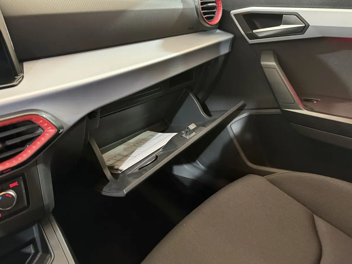 Vue intérieure côté passager de la SEAT Ibiza 2024, boîte à gants ouverte avec documents visibles, ambiance noire et grise.