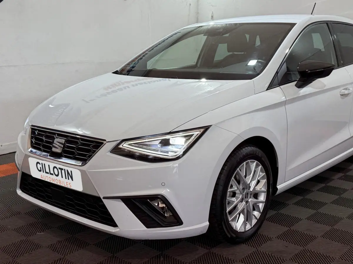 SEAT Ibiza 1.0 TSI 110 FR blanc vue 3/4 avant droit, phares LED allumés et jantes alliage distinctives.
