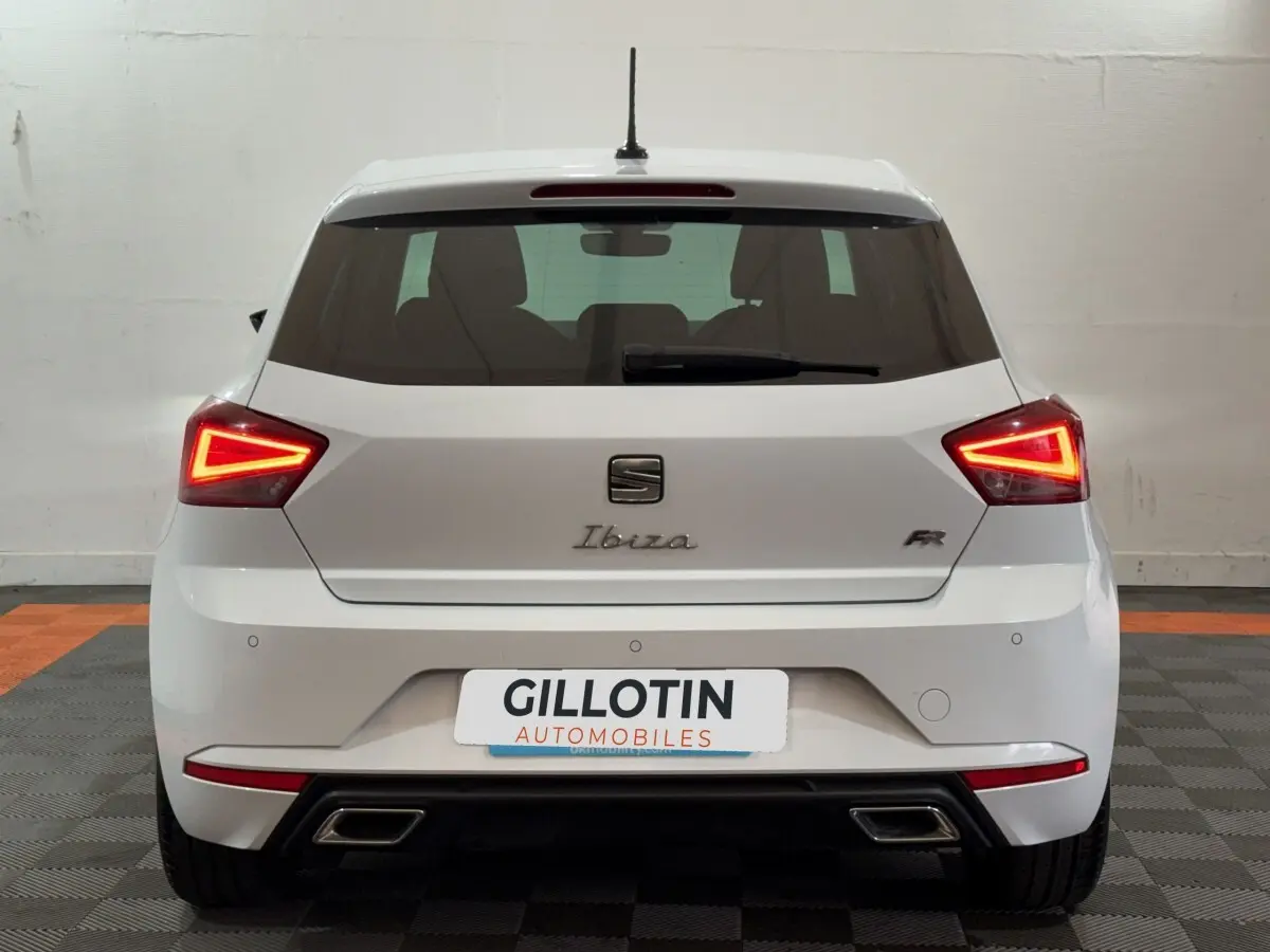 Vue arrière d'une SEAT Ibiza 1.0 TSI 110 FR blanche avec feux LED triangulaires allumés et double sortie d'échappement.