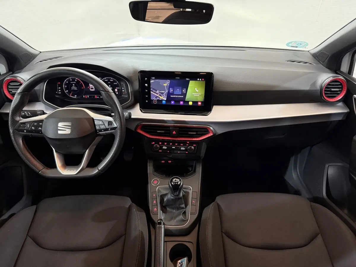 Vue intérieure avant de la SEAT Ibiza 2024, tableau de bord noir avec touches rouges et écran tactile central.