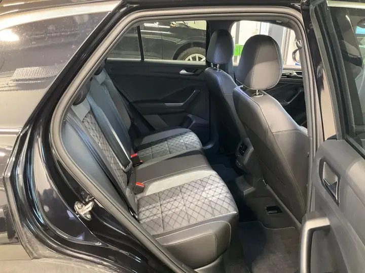Vue intérieure du côté arrière gauche du Volkswagen T-Roc noir intense 2025, mettant en valeur les sièges arrière en tissu et cuir avec surpiqûres.