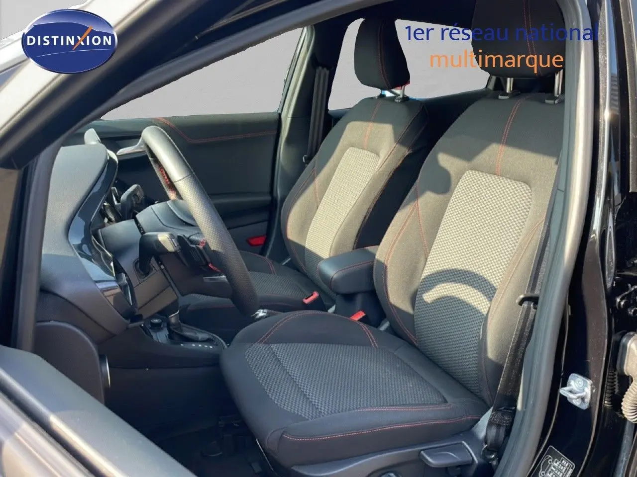 Intérieur avant du Ford Puma noir agate métal 2023, sièges tissu avec surpiqûres rouges et volant multifonction.