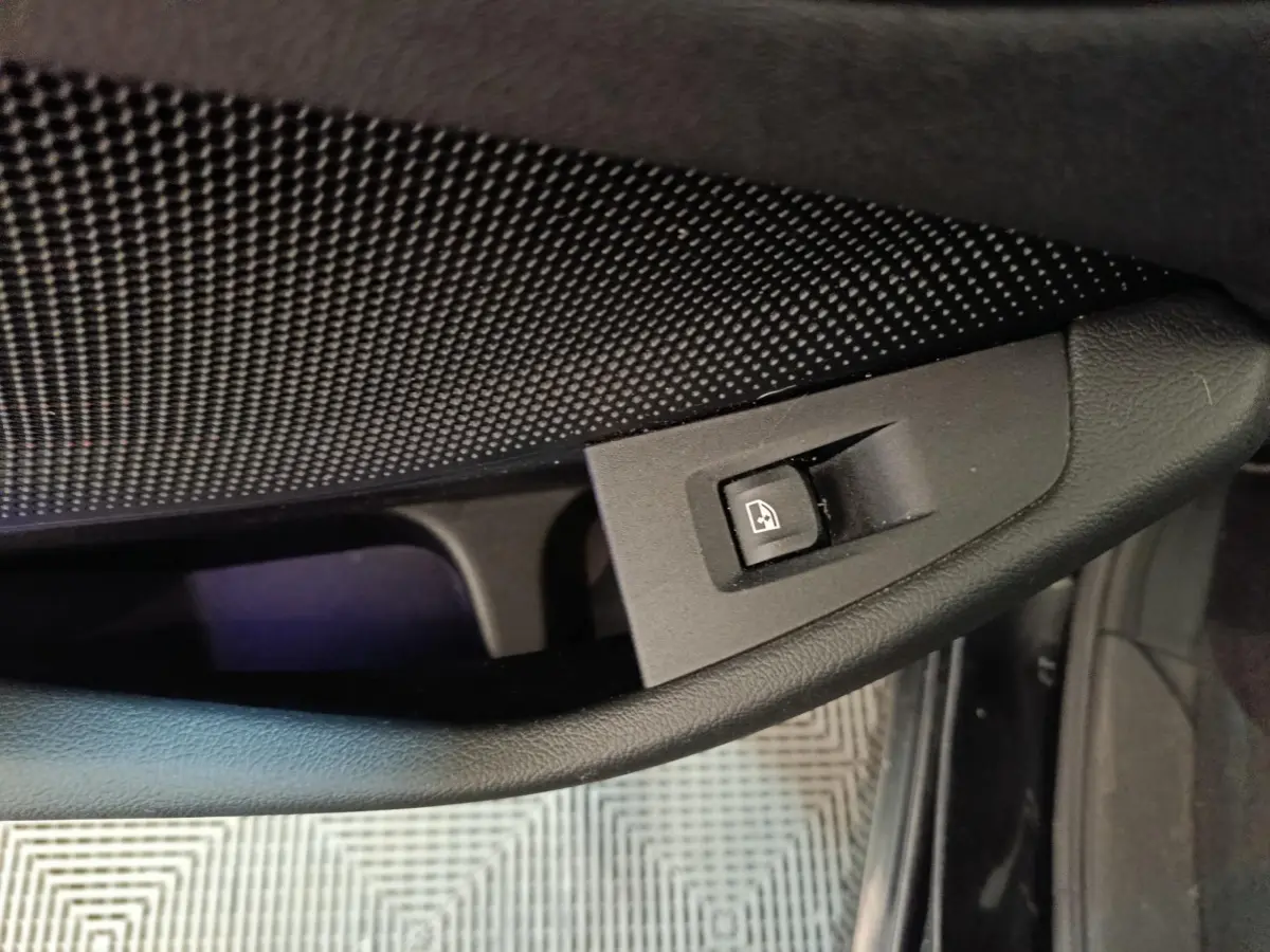 Gros plan sur la commande de lève-vitre côté conducteur de la BMW Série 1 118i noire, intérieur sombre.