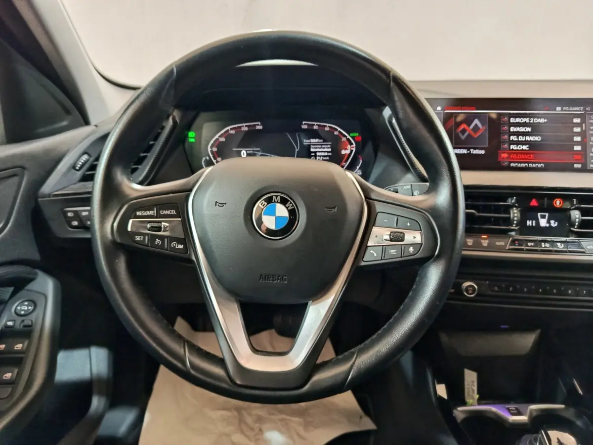 Vue intérieure centrée sur le volant cuir noir et le tableau de bord numérique de la BMW Série 1 118i Edition Sport 2023.