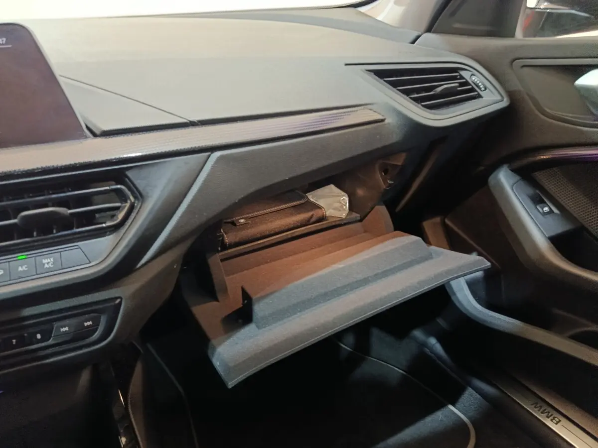 Intérieur BMW Série 1 118i Edition Sport 2023, vue côté passager sur boîte à gants ouverte et tableau de bord noir.