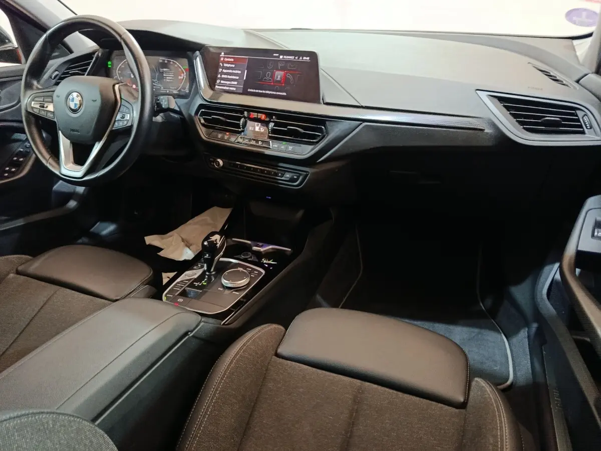 Intérieur BMW Série 1 118i Edition Sport 2023, vue de face côté conducteur, tableau de bord et console noire moderne.