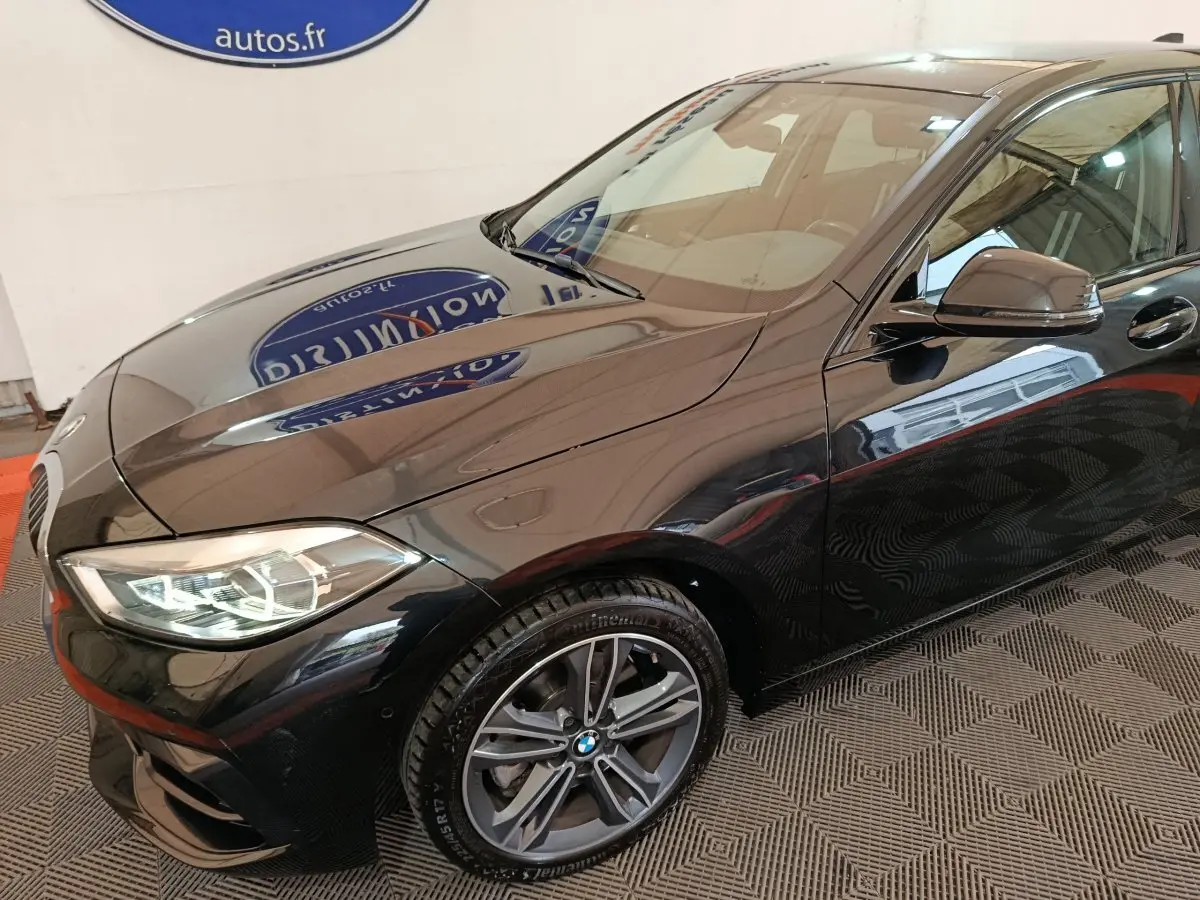 BMW Série 1 118i Edition Sport noire vue 3/4 avant droit, avec phares LED et jantes alliage visibles.