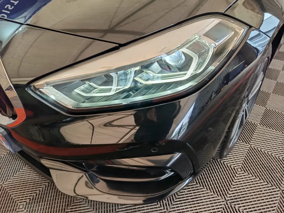 Gros plan sur le phare avant droit noir brillant d'une BMW Série 1 118i Edition Sport 2023.