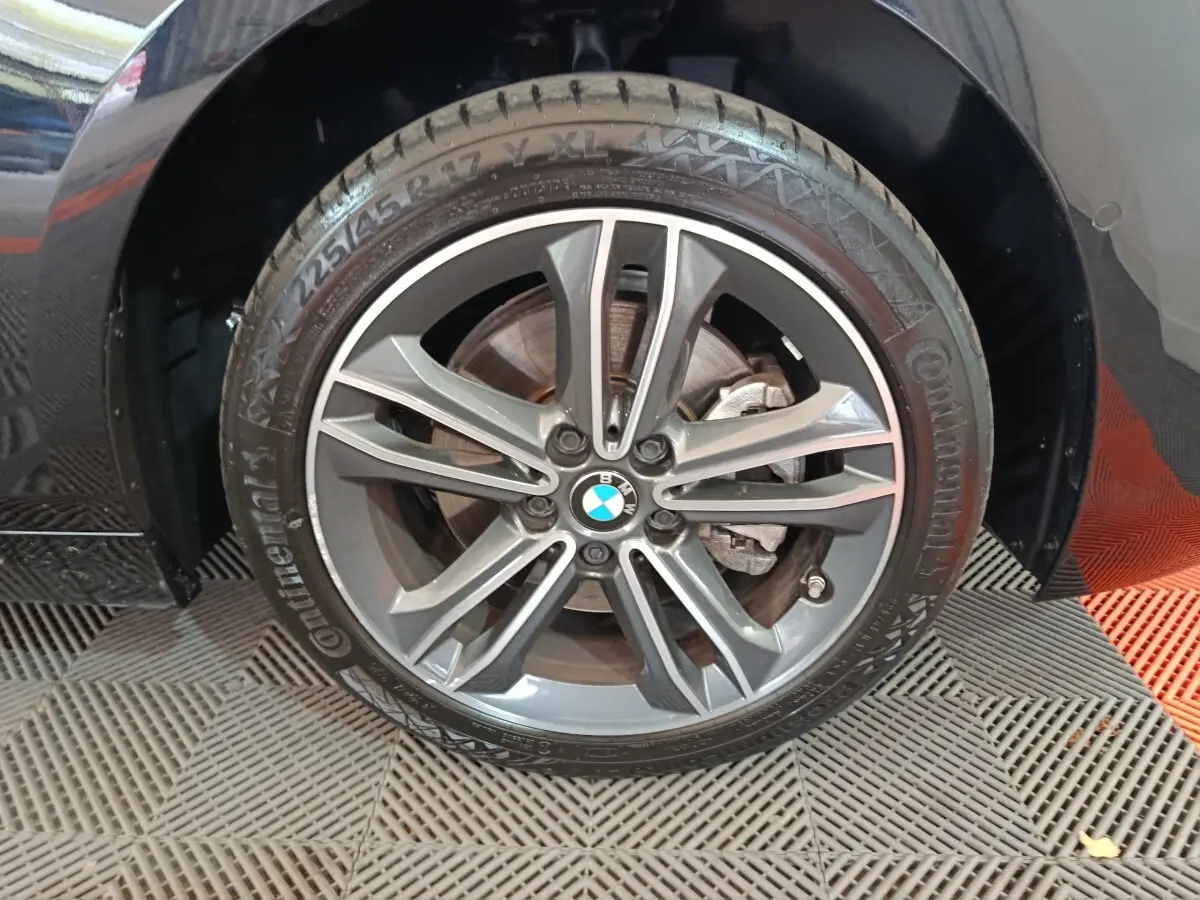 Gros plan sur la roue avant gauche noire d’une BMW Série 1 118i Edition Sport avec jante alliage grise.