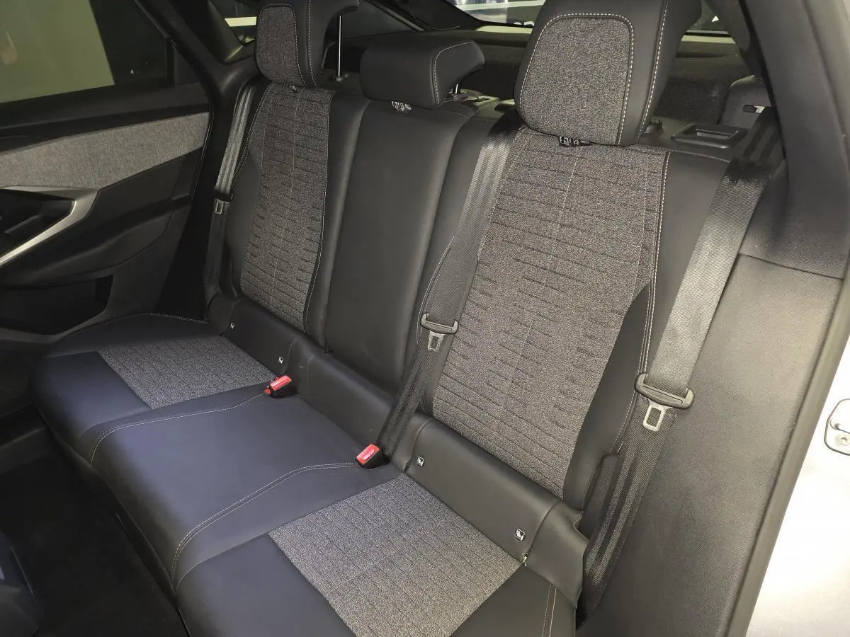 Vue latérale droite de la banquette arrière gris tissu et noir cuir du Peugeot 3008 2025 hybride avec ceintures de sécurité visibles.